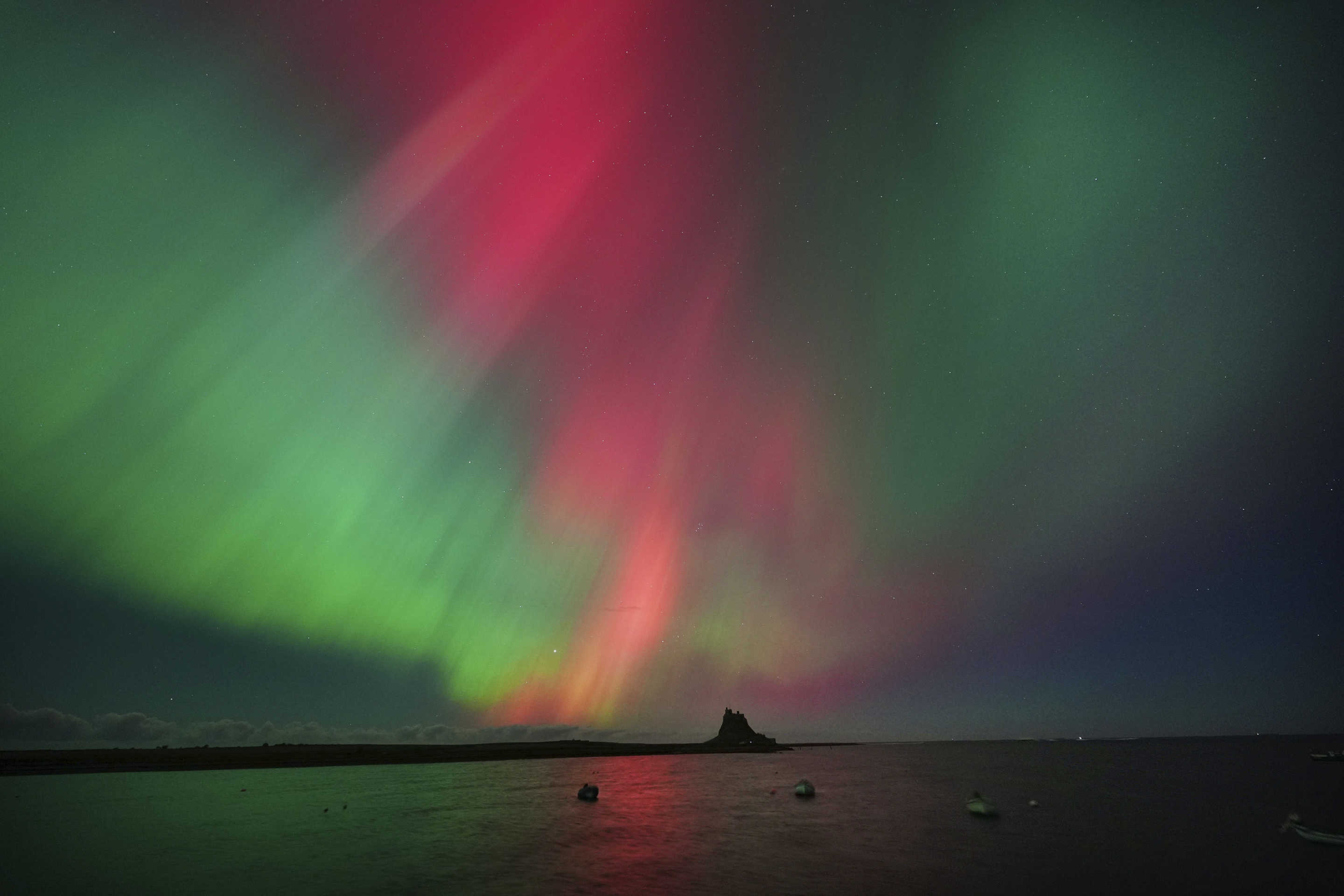 Aurora borealis against body of water with distant land mass.