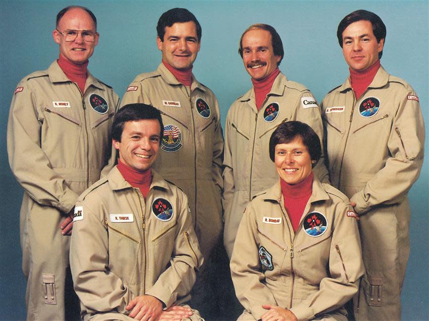 six astronauts in flight suits smiling at a camera