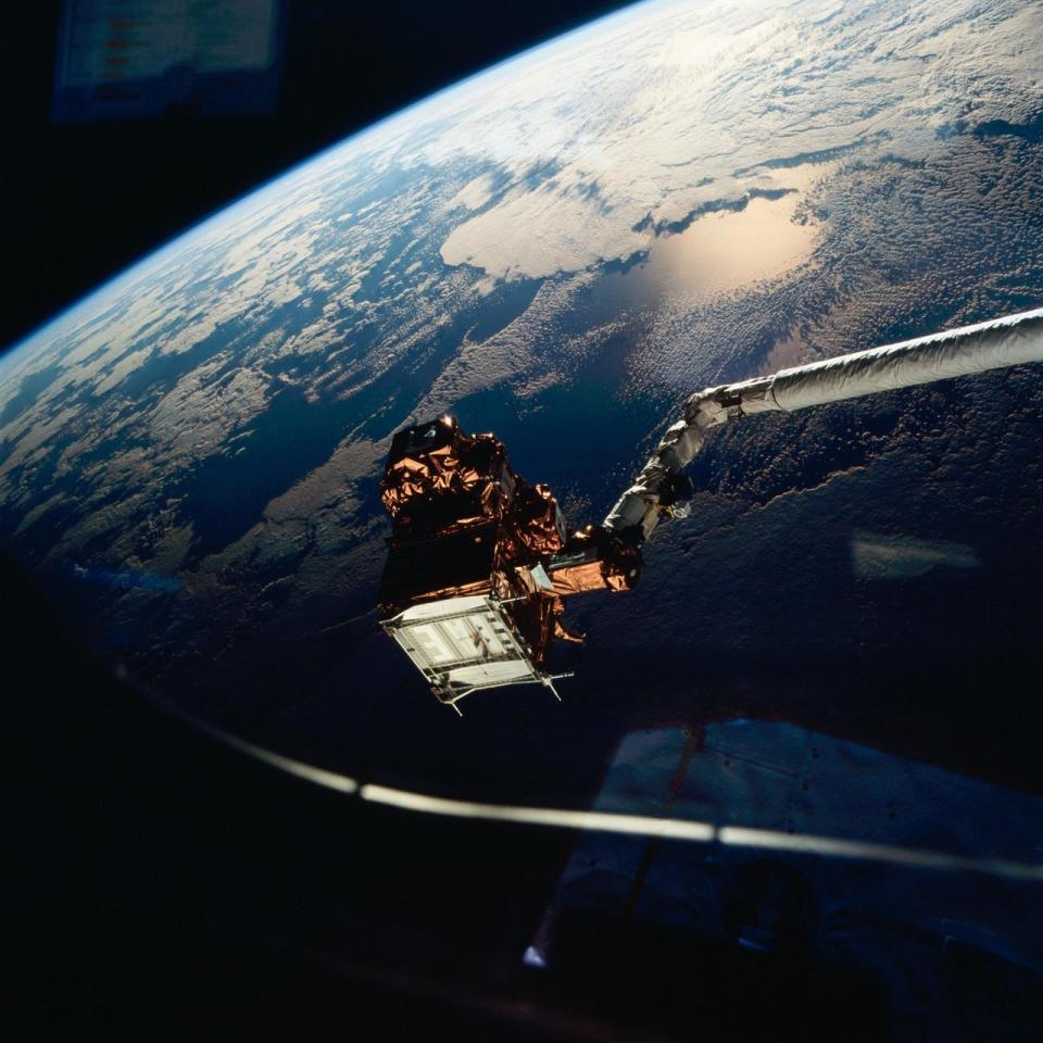 a satellite with canadarm backdropped by earth and the curve of space