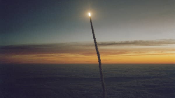 a rocket launch seen from afar as the sun is rising in the background