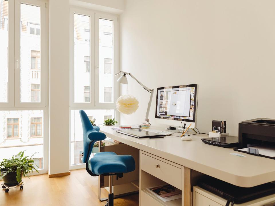 A home-office setup with a desk, computer, lamp, decor, and a blue chair next to floor-to-ceiling windows.