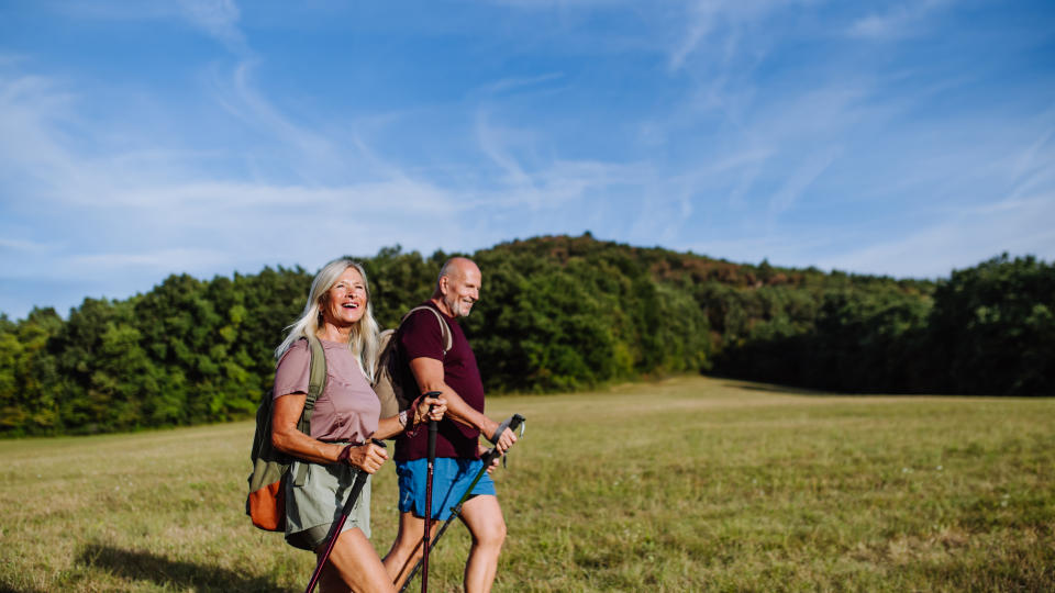 Active senior couple spending their free time outdoors, hiking in nature. Senior man and woman with trekking poles and backpack.