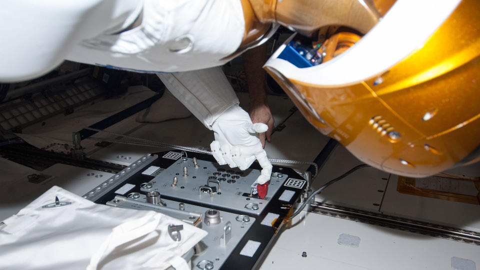 closeup of a white humanoid robot with a gold helmet flipping a switch aboard the international space station