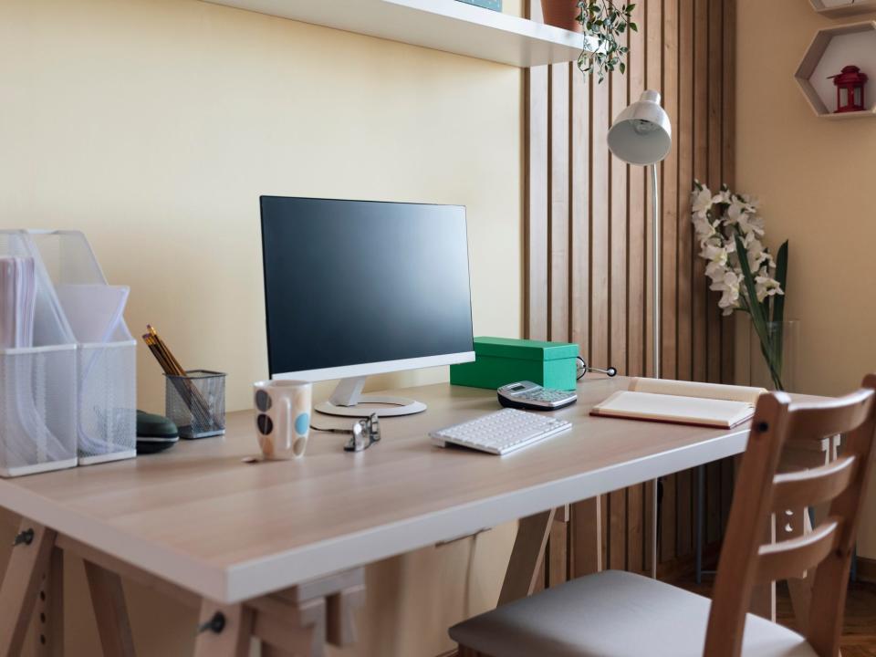 A chair and a desk with a computer, mug, glasses, filing containers, a pencil organizer, a calculator, and a planner.