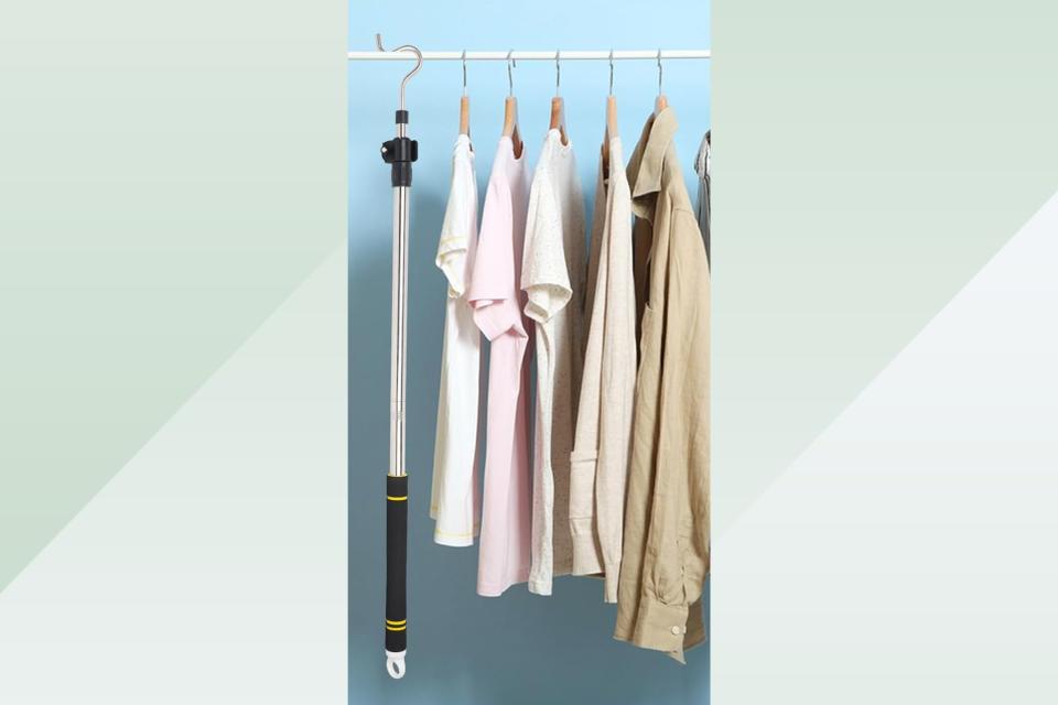 A closet rod with clothes and the hook pole hanging off of it on a green background. 