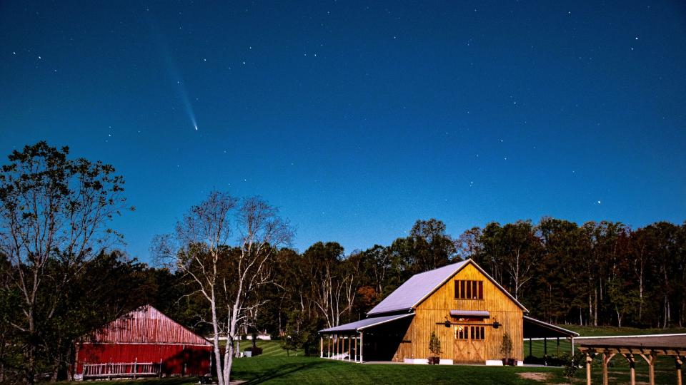  A fuzzy white streak in the night sky above a red barn. 