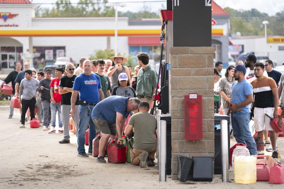 Dozens of people wait with hand-held gas canisters to fill them at a gas station.