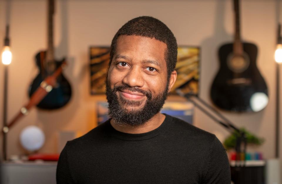 Tristan Thomas smiling and wearing a black-tshirt with guitards behind him