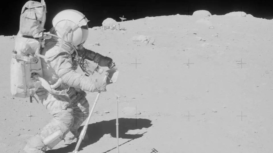  An astronaut in a bulky white suit walks on the dusty grey surface of the moon. 