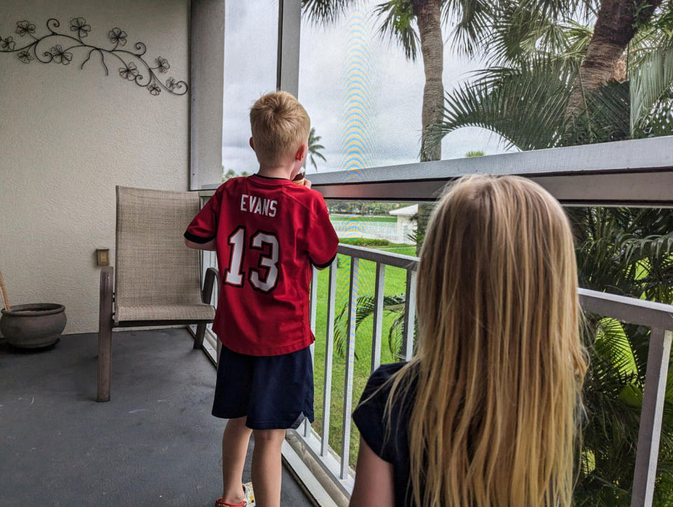 Two children look beyond the fence of a porch on a cloudy day (Michelle Chernicoff)