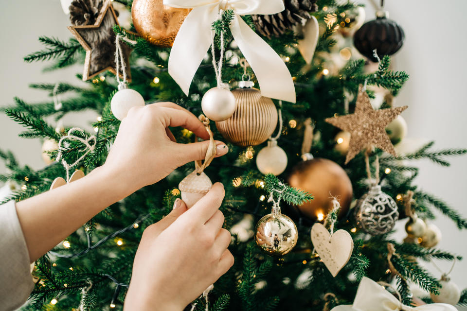 Hands decorating a Christmas tree with ornaments and garland