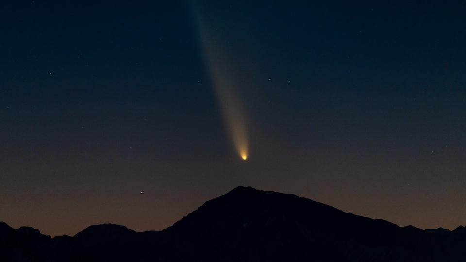  A fuzzy bright orb leaves a trail behind it in the night sky above the silhouette of a mountain. 