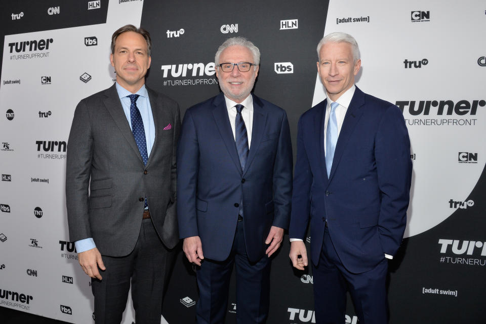 Jake Tapper in a gray suit and tie, and Wolf Blitzer and Anderson Cooper in navy-blue suits, pose in front of a wall marked Turner Upfront.