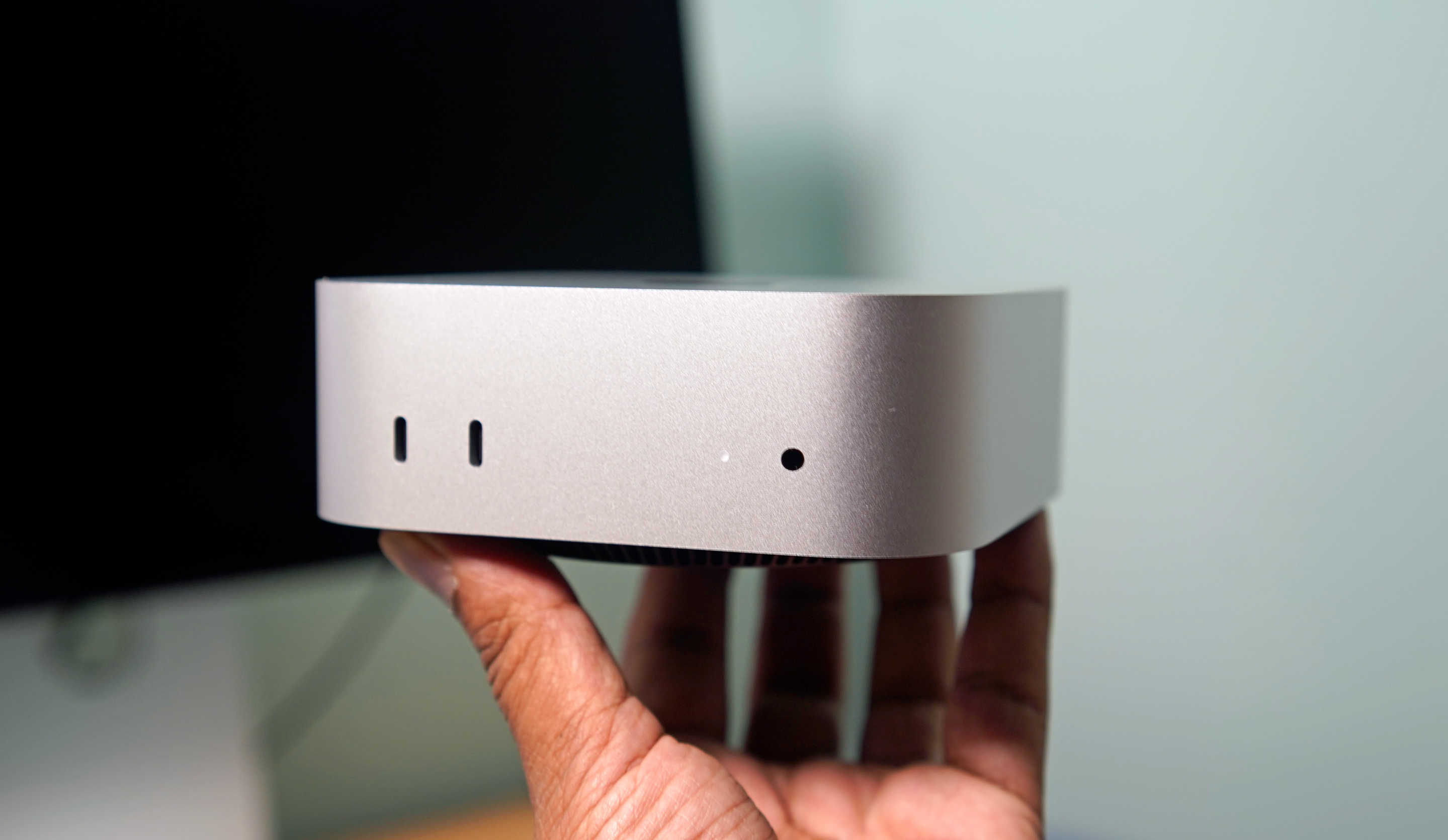 Apple Mac mini (2024) in hand, viewing the USB-C ports and headphone jack up front