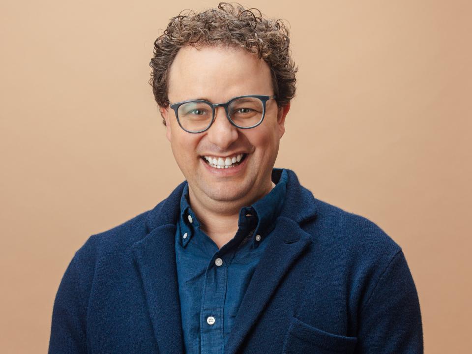 Dario Amodei, the CEO of Anthropic, sits in front of a tan background.