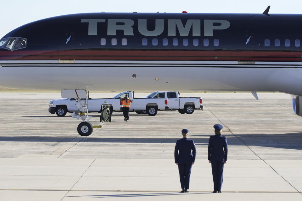 Two women in blue uniforms stand to attention in front of a plane marked Trump.