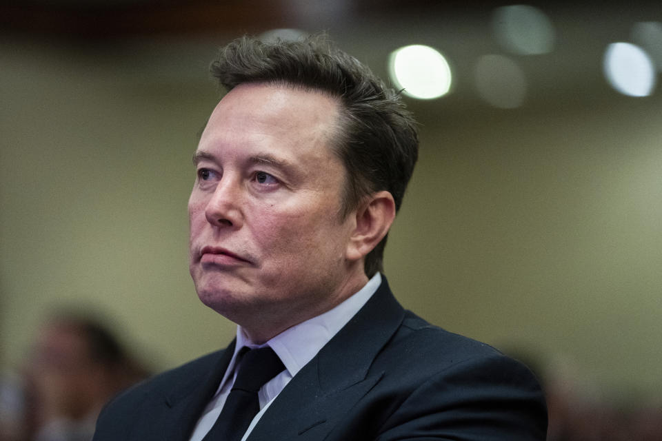 Elon Musk, looking serious, with set jaw, listens.