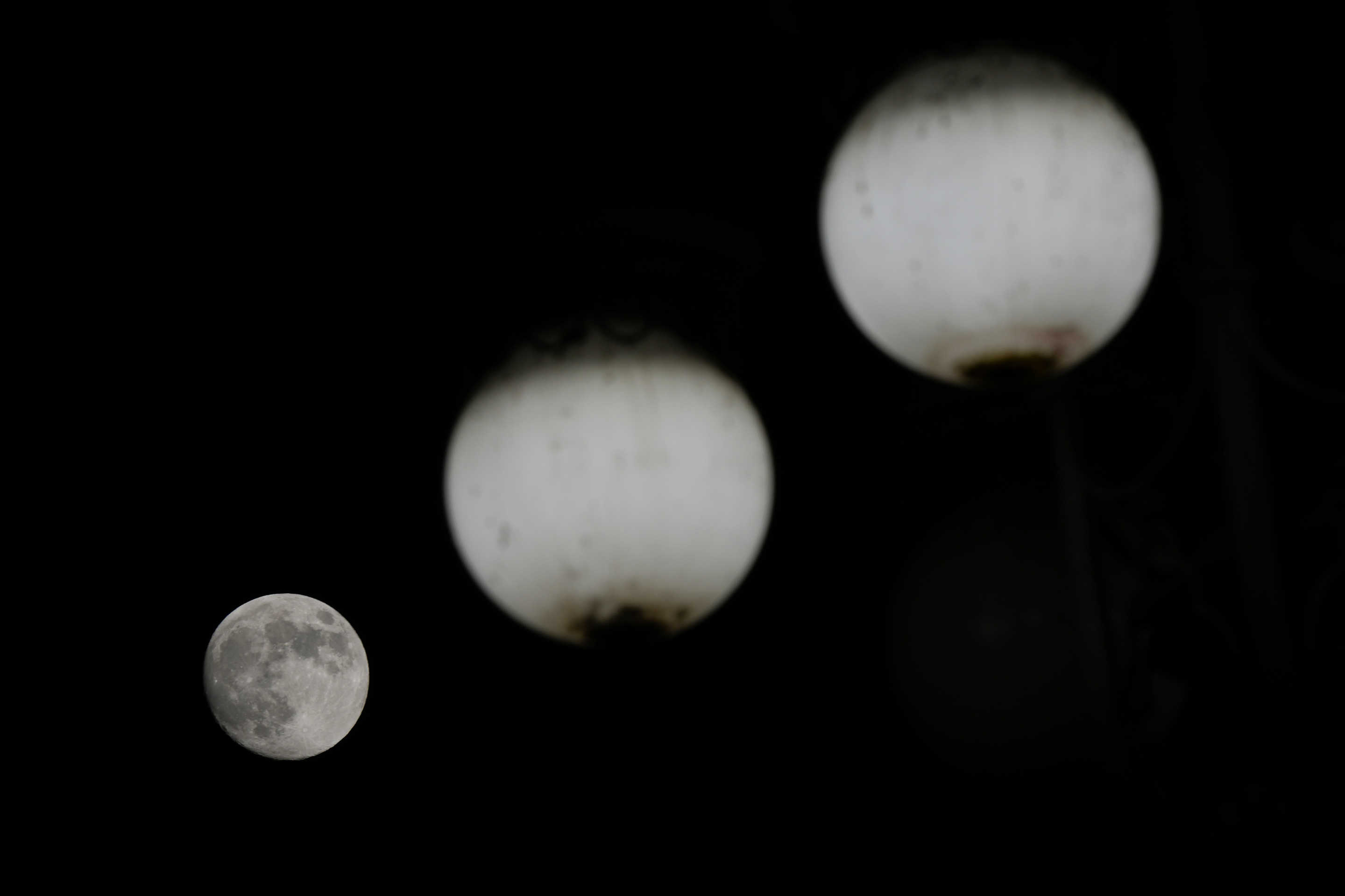 The moon rises behind street lamps in Milan on Thursday.