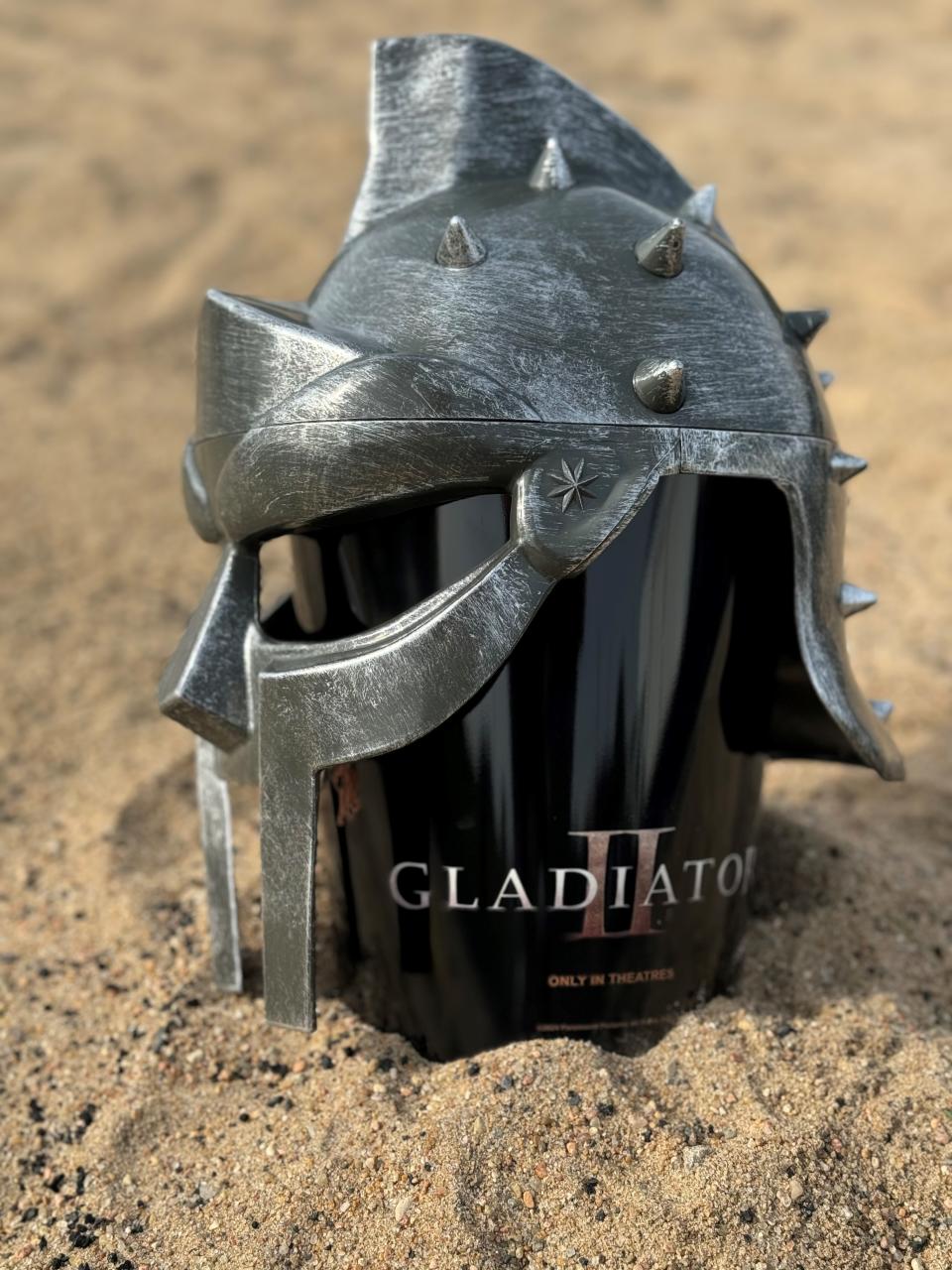 A helmet-covered popcorn bucket sits in sand.