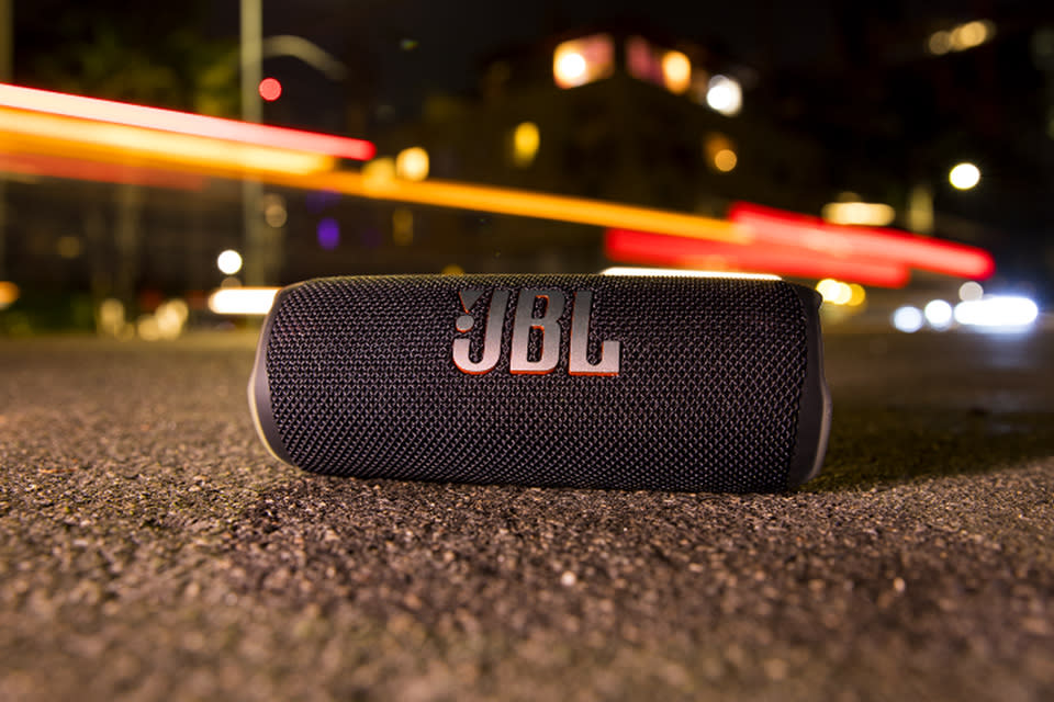 The JBL Flip 6 sits on the pavement on a city street at night. 