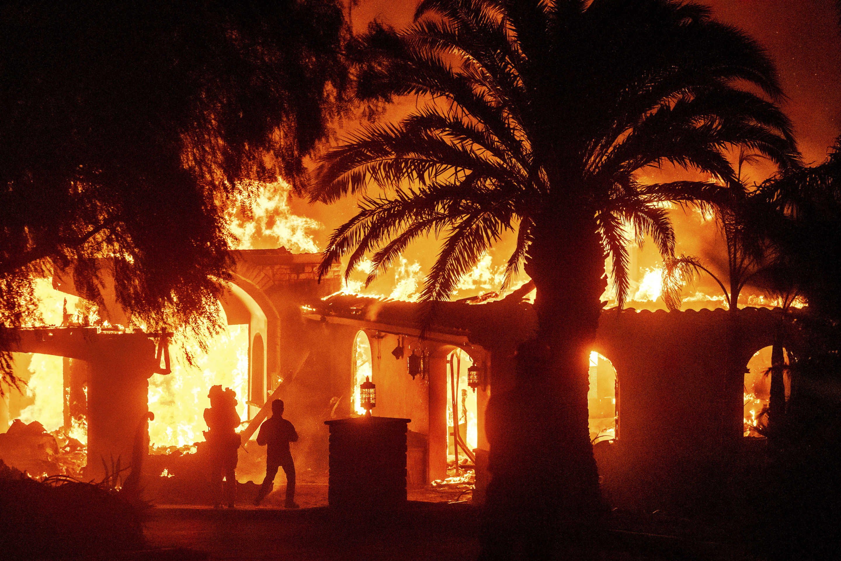 A person's silhouette can be seen against flames from the Mountain Fire as it consumes a home in Camarillo, Calif.