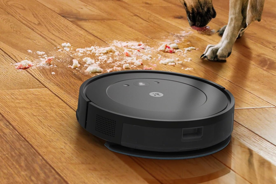 The iRobot Roomba robot vacuum and mop cleaning spilled food on a wooden floor next to a dog