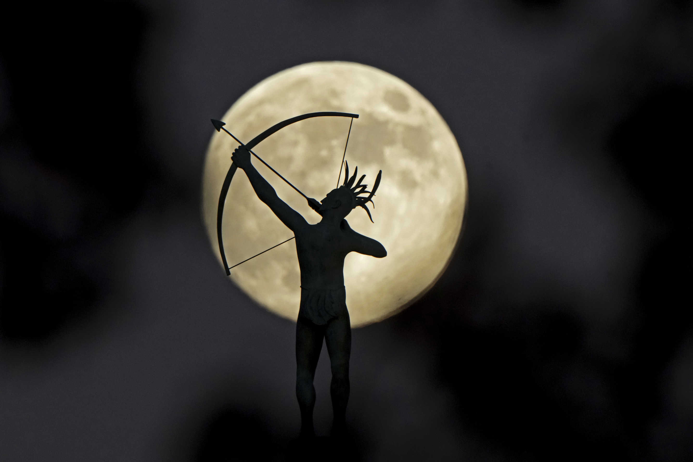 A bronze sculpture of Ad Astra, a Kansa Indian, perched atop the Kansas Capitol dome is silhouetted against the nearly full moon on Thursday in Topeka, Kan.