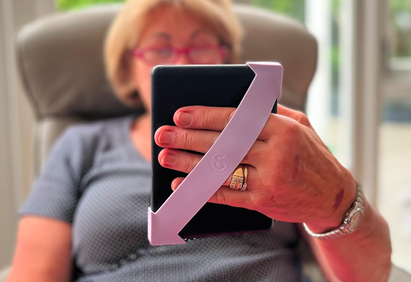 Woman using Strapsicle Hand Strap for Kindle while reading