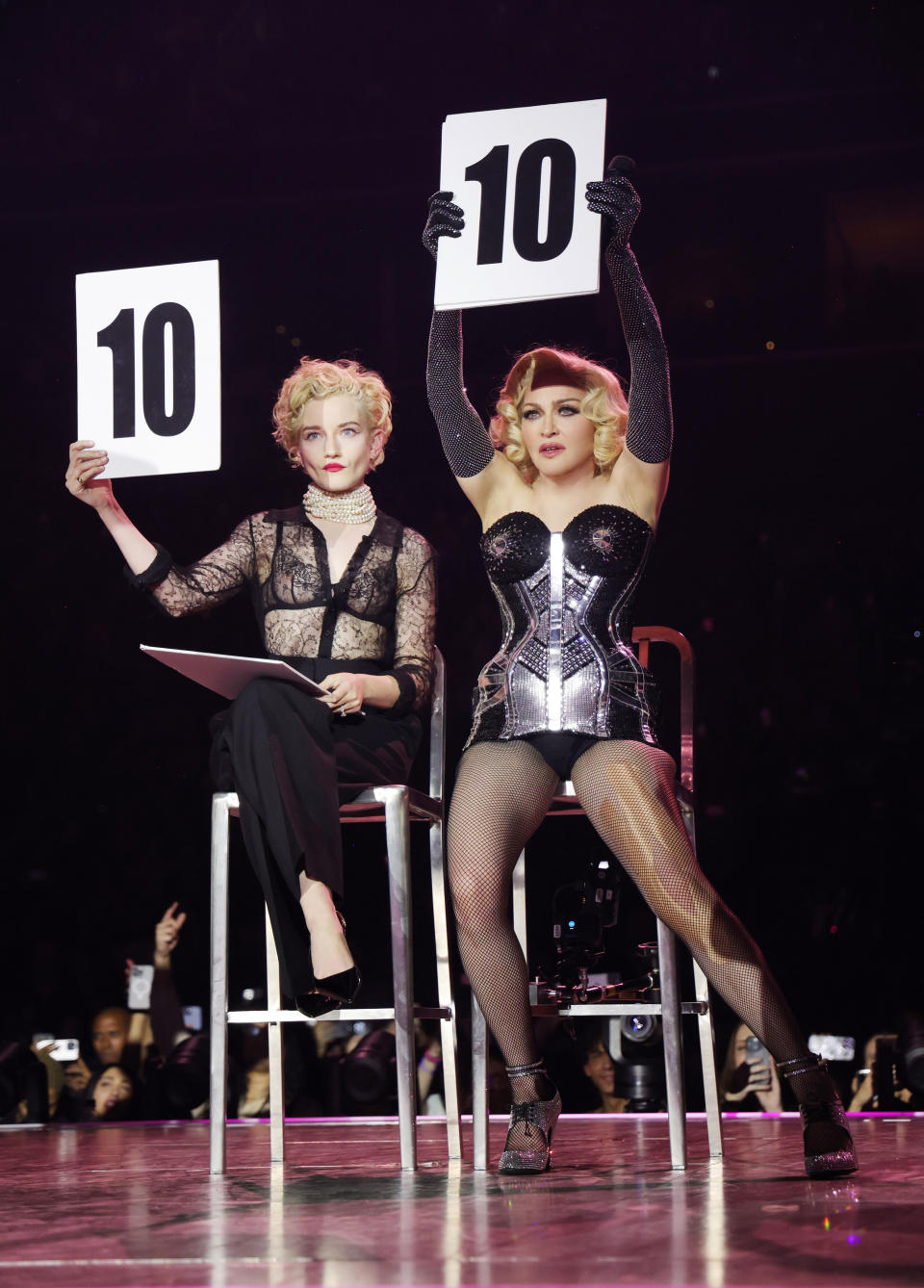 Garner, seated on high chair, wearing black paints and a see-through top, holds up a 10, as does Madonna, stands by her side in a bustier, long black gloves and fishnet stockings.