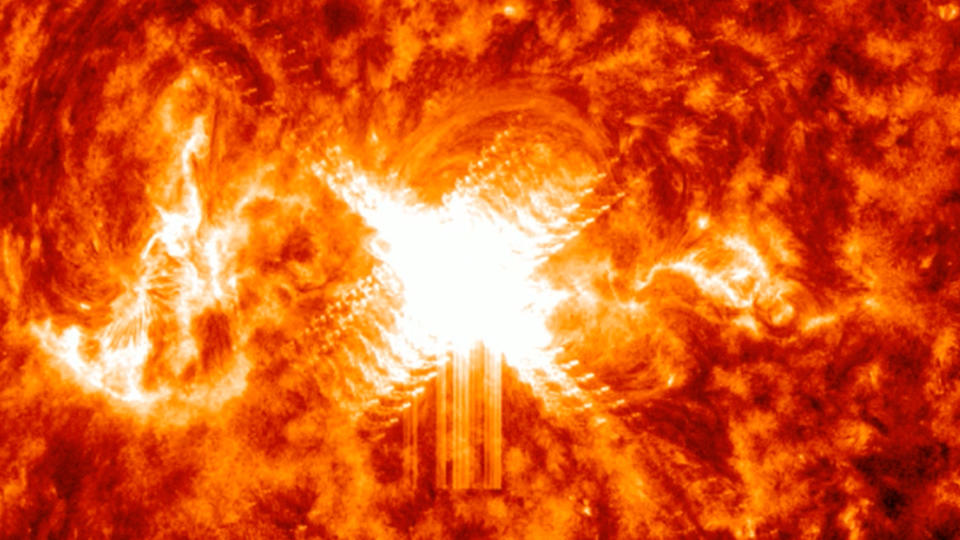  A giant white flare, like an X bursts from the center of a fiery surface, blazed with reds and oranges in a swirling inferno. 