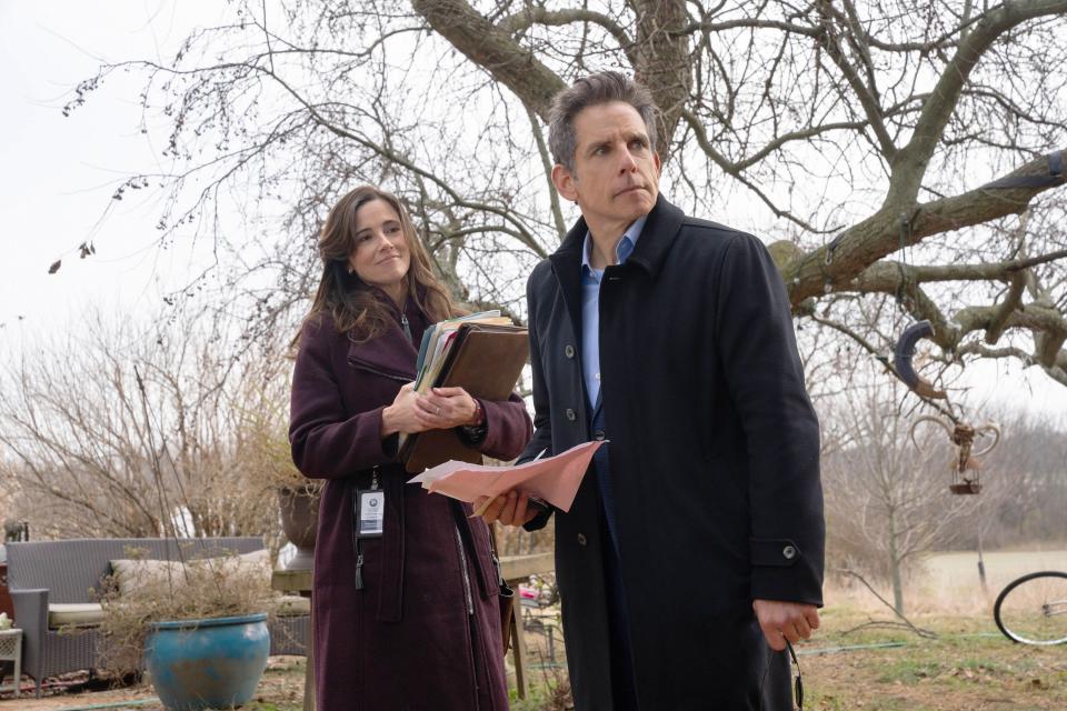 Linda Cardellini looks on, amused, in a field in winter, as Ben Stiller stares into the distance.  