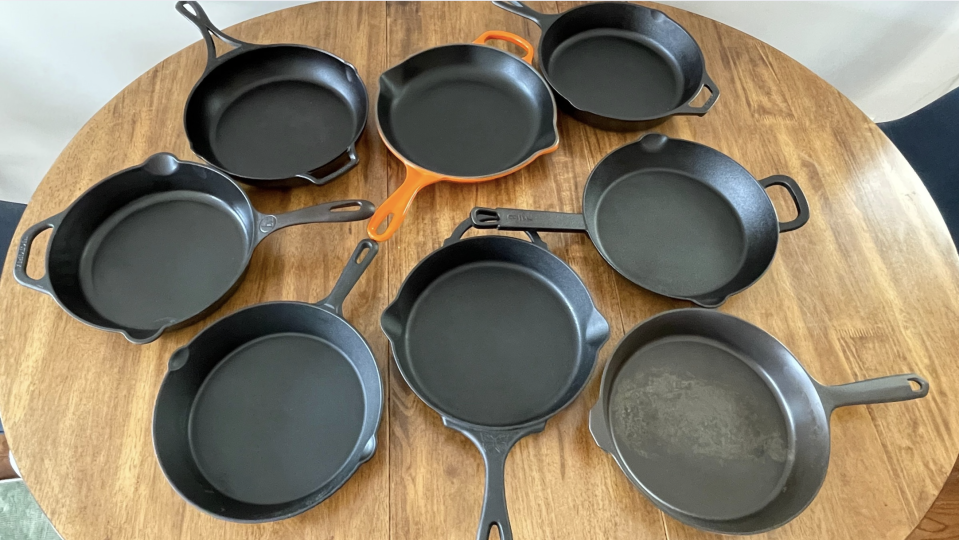 Eight cast iron skillets on a wood table