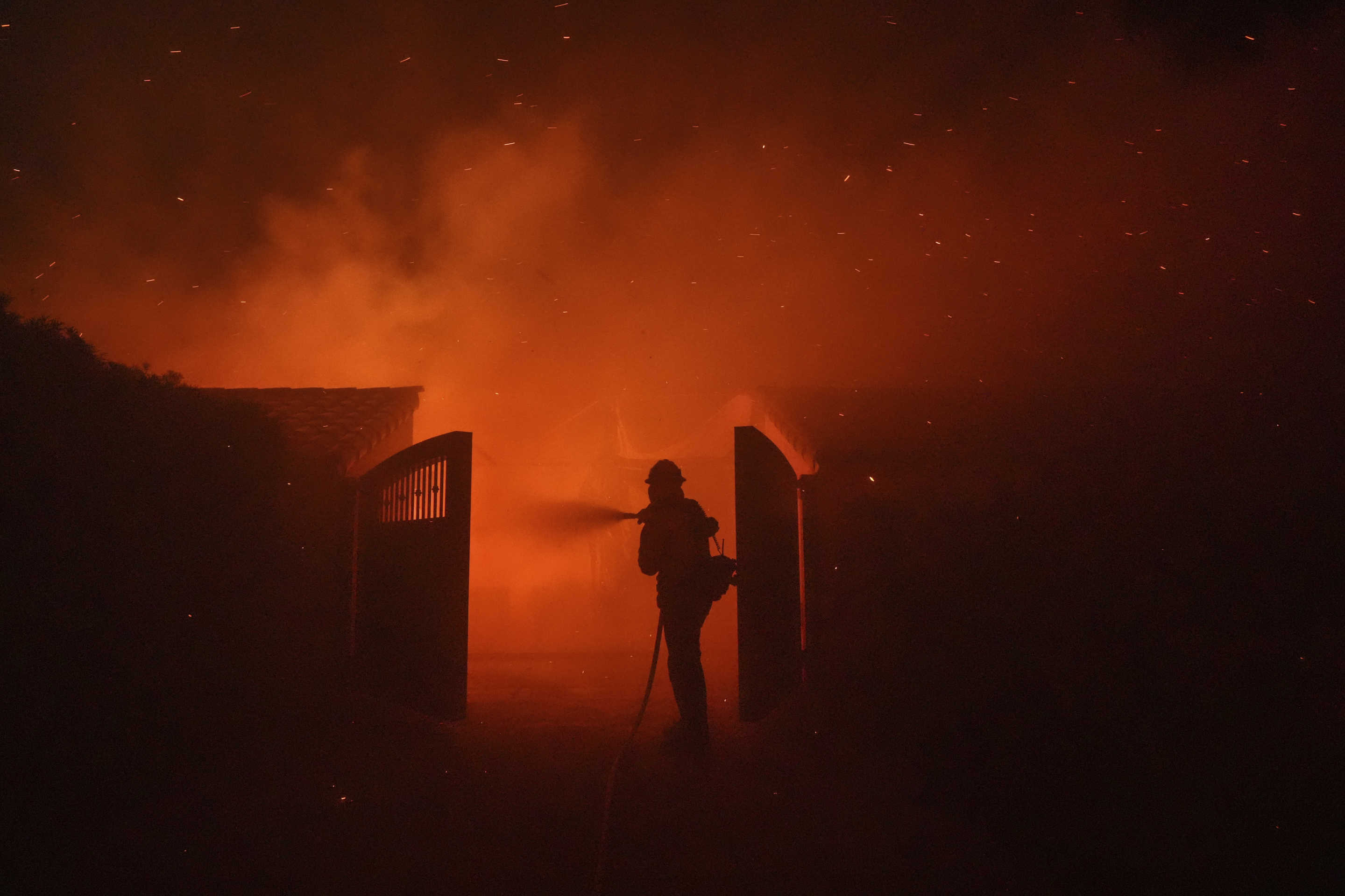 A firefighter behind an open gate hoses a building.