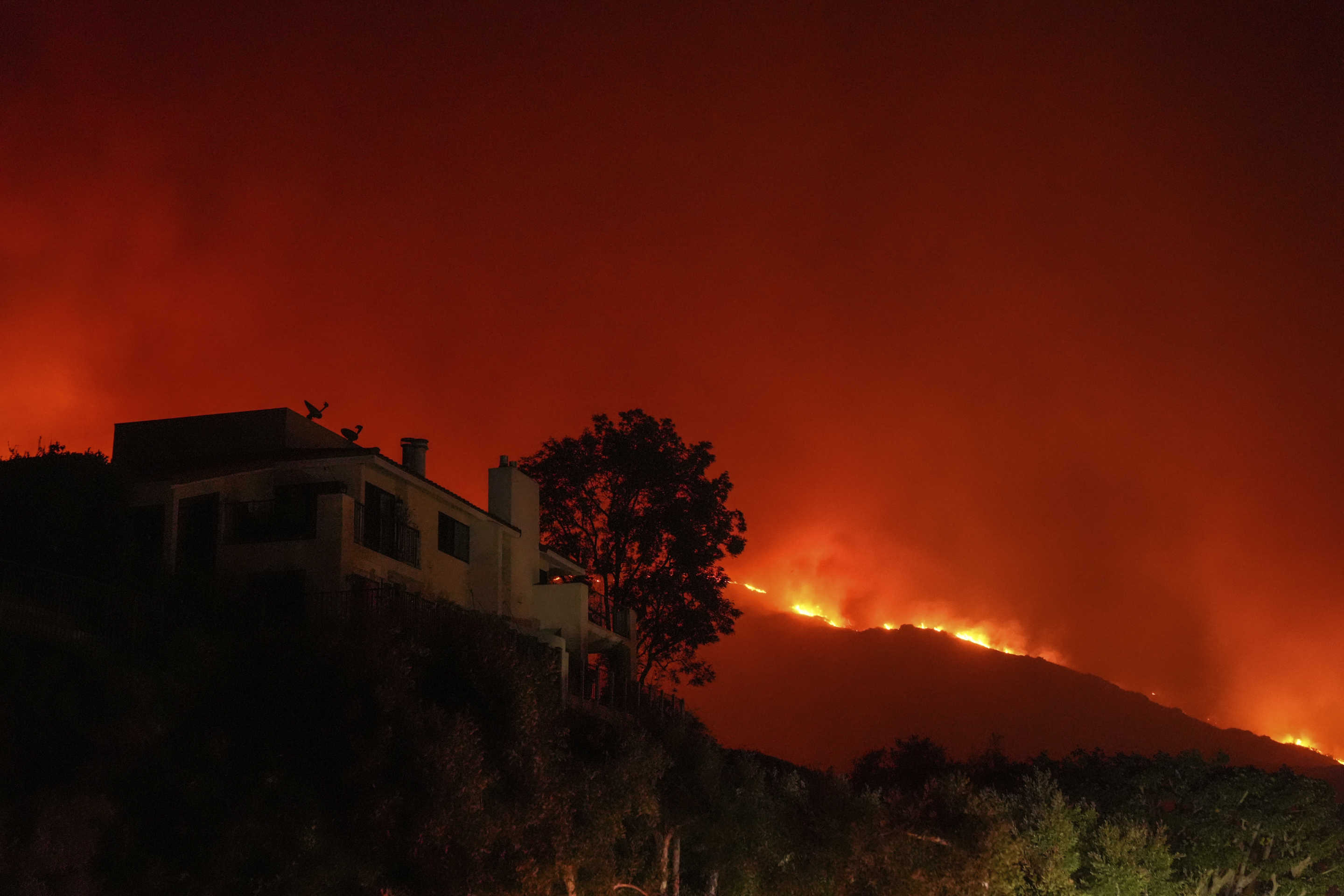 Flames lick up the crest of a hill toward a building.