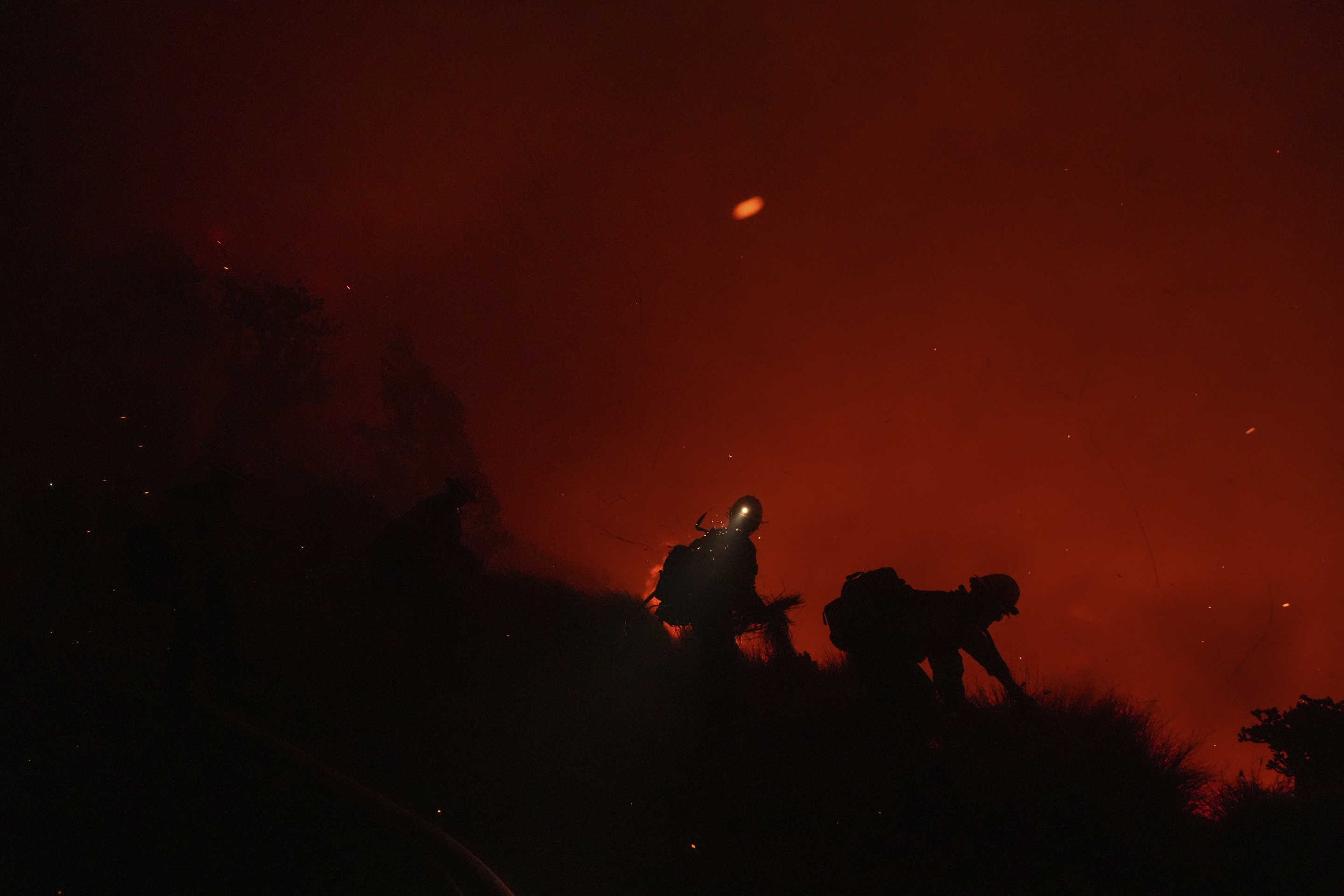 Firefighters silhouetted against a hillside remove vegetation.