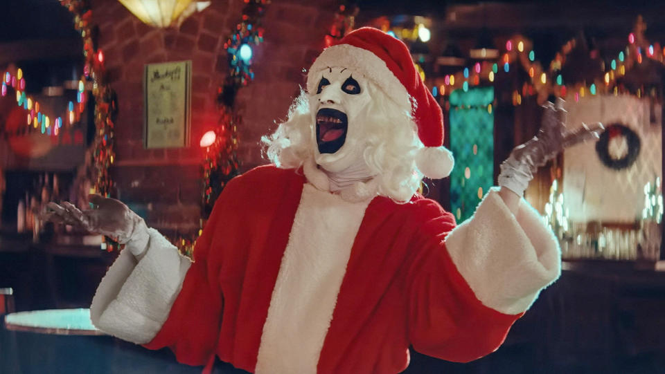 David Howard Thornton in a Santa outfit with a huge beaky mask and gaping mouth edged in black.