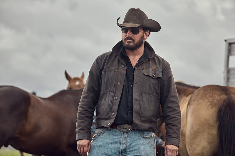 Cole Hauser posed for action in manly stance with the flanks of two horses ins the background.