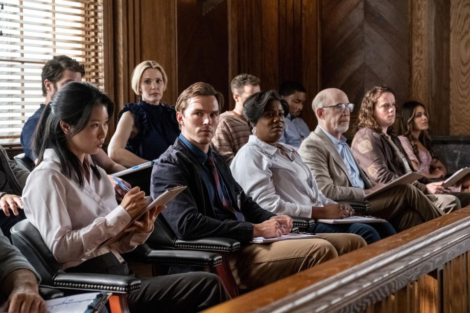 Nicholas Hoult, eyes to the camera and looking apprehensive, sits with the other jurors, who are facing straight ahead..