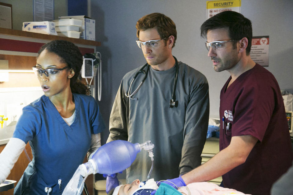 Yaya DaCosta, Nick Gehlfuss, Colin Donnell, in scrubs, stand over a patient, looking over to their instruments. 