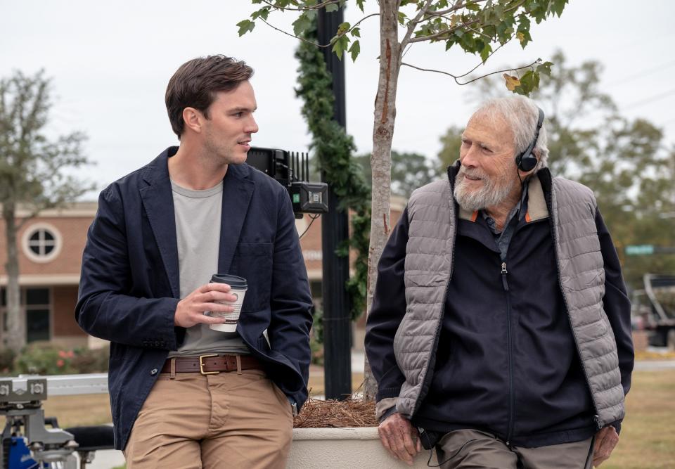 Nicholas Hoult, holding a paper cup of coffee, has a friendly exchange with Clint Eastwood, who is wearing earphones. 