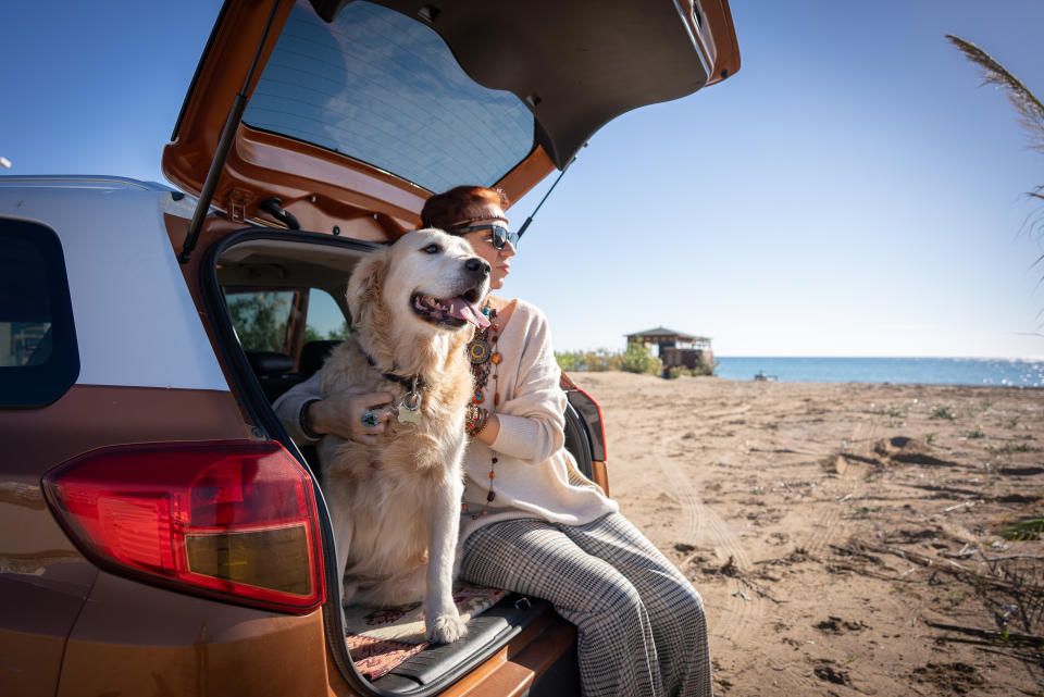 Bohemian woman and her cute dog in a car on the beach. Travel concept.