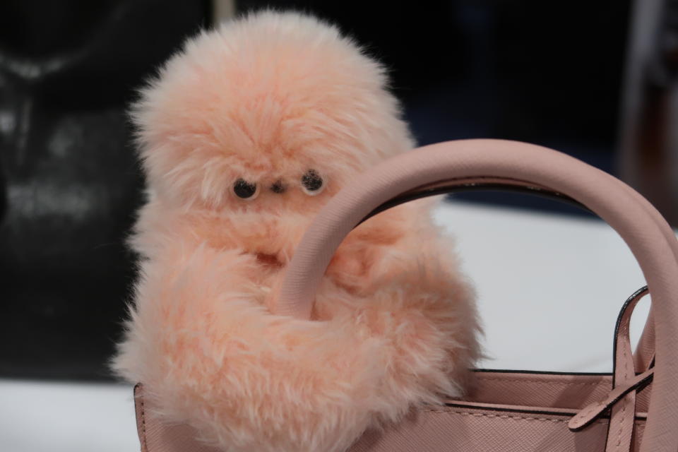 A peach colored bird like robot with long arms is shown clinging onto a pink purse handle