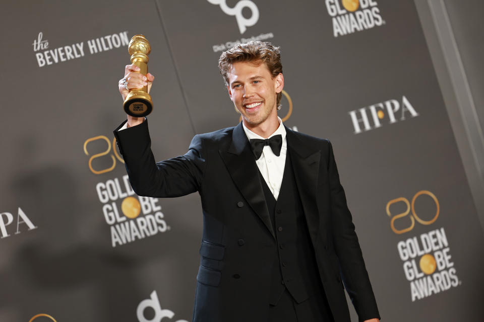 Austin Butler poses with the Best Actor in a Motion Picture – Drama award in front of a wall advertising the Golden Globe Awards. 