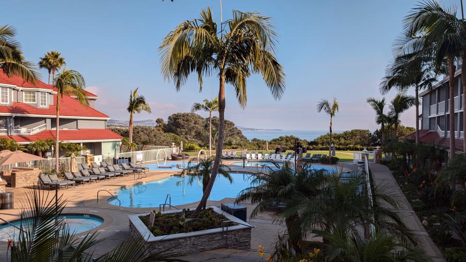 a view of a hotel swimming pool and hot tub with palm trees and the ocean in the background