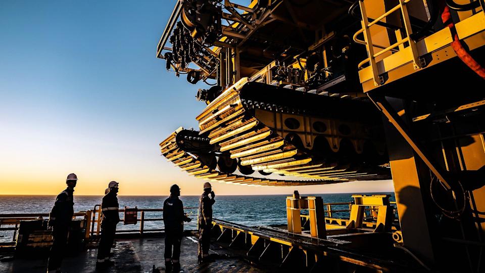 The crew of a ship look up at the tracks of a subsea mining vehicle.