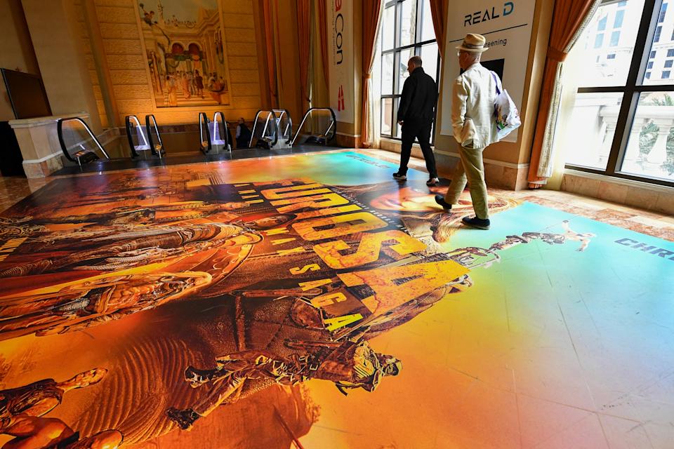 People walk on a floor poster of Furiosa: A Mad Max Saga during CinemaCon 2024.