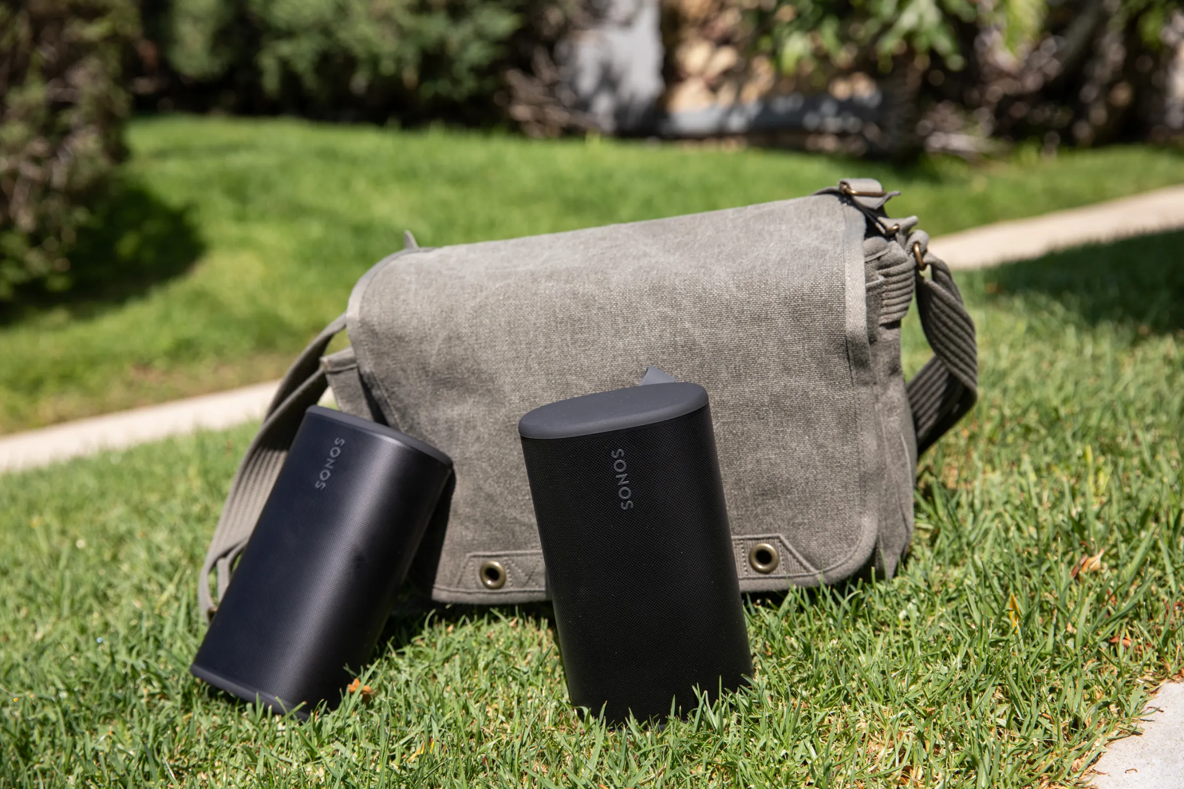 Two Sonos Play speakers positioned on grass in front of a sage colored bag in a 2026 setting
